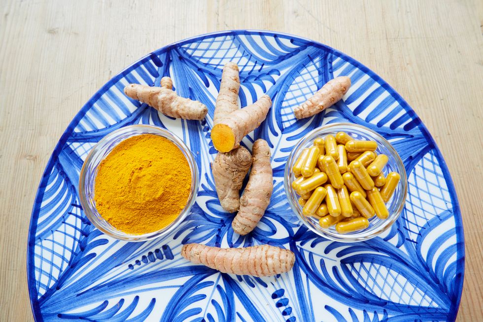 Turmeric, turmeric pills and turmeric powder lay on a blue floral painted table